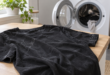 Maglia nera con residui chiari di lavaggio appoggiata accanto a una lavatrice con oblò aperto