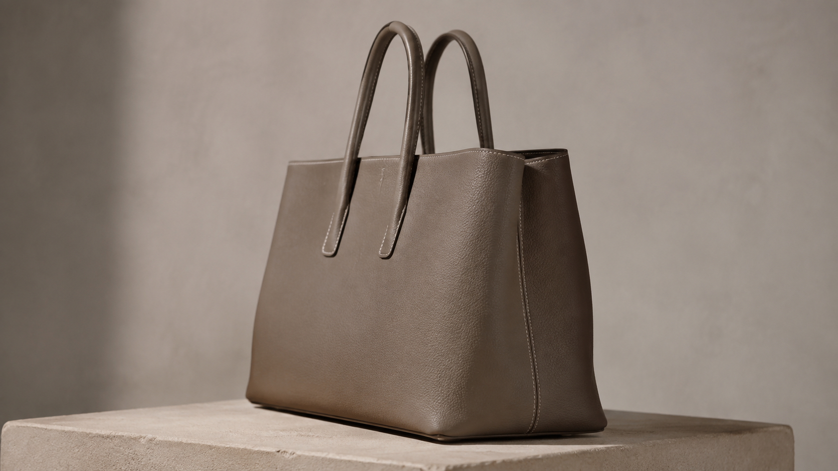 Borsa strutturata senza marchi in pelle color tortora su un piedistallo in pietra